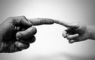 Eine Hand eines Erwachsenen und eines Kindes, beide haben ausgestreckte Zeigefinger, die sich berühren